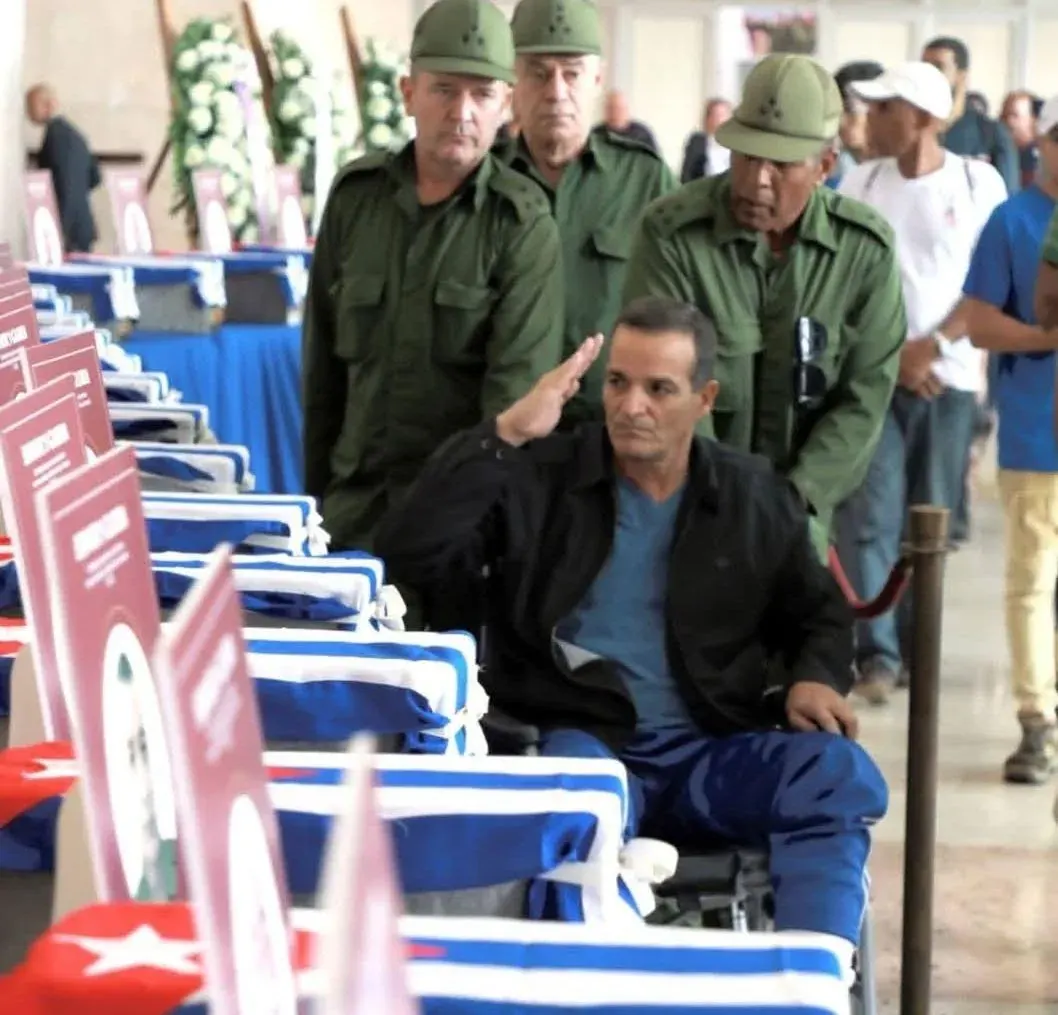 Funeral ceremony with coffins draped in Turkish flags, a man in a wheelchair saluting, and uniformed guards standing nearby Funeral ceremony with coffins draped in Turkish flags, a man in a wheelchair saluting, and uniformed guards standing nearby