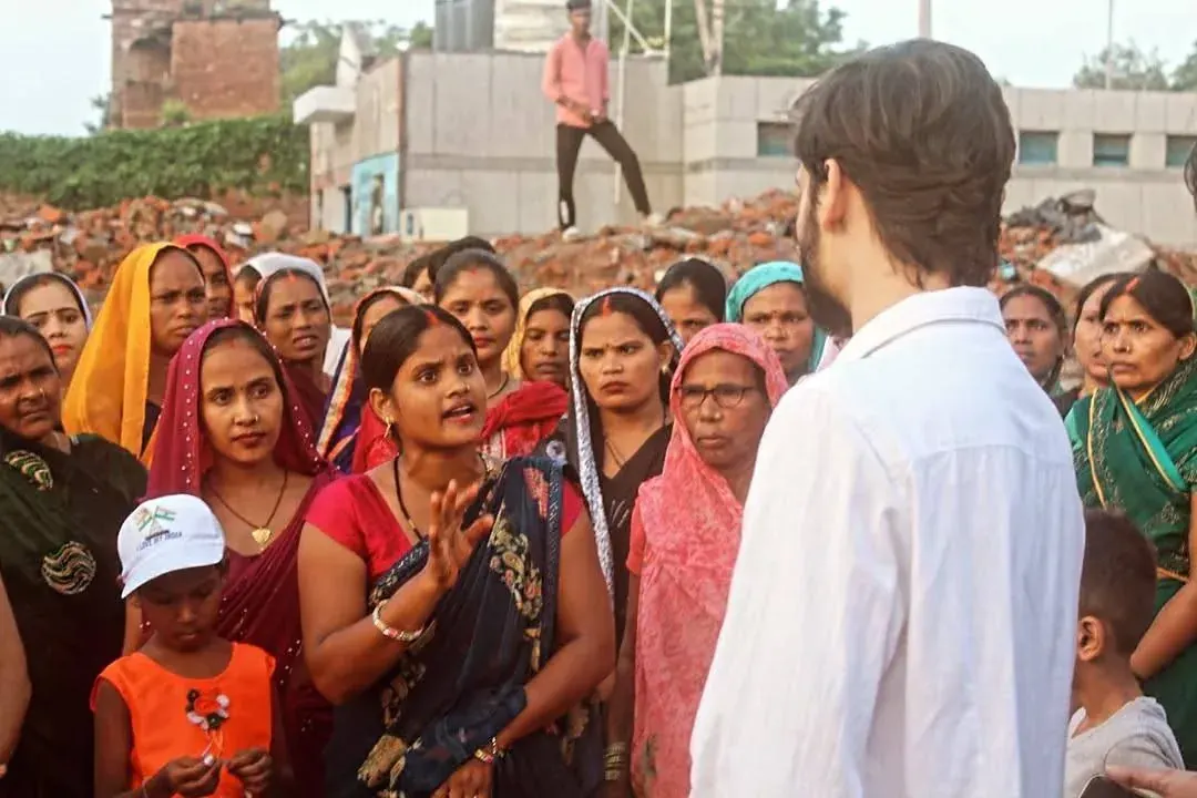 A man speaks to a gathered community of South Asian women and children in an outdoor civic discussion setting A man speaks to a gathered community of South Asian women and children in an outdoor civic discussion setting